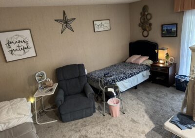 A neatly arranged bedroom with a single bed, recliner chair, nightstand, walker, and wall decor featuring inspirational quotes.
