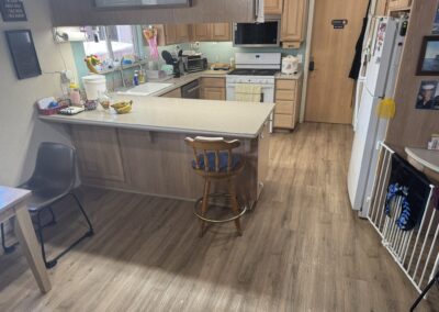 A kitchen with wooden cabinets, a white stove, refrigerator, and microwave, a central island with a wooden chair, and various small appliances and items on the counters.