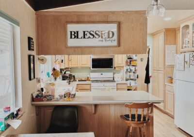 A cozy kitchen with wooden cabinets and ceiling, a white refrigerator, a microwave, and a sign above the counter that reads “BLESSED and Grateful.”.